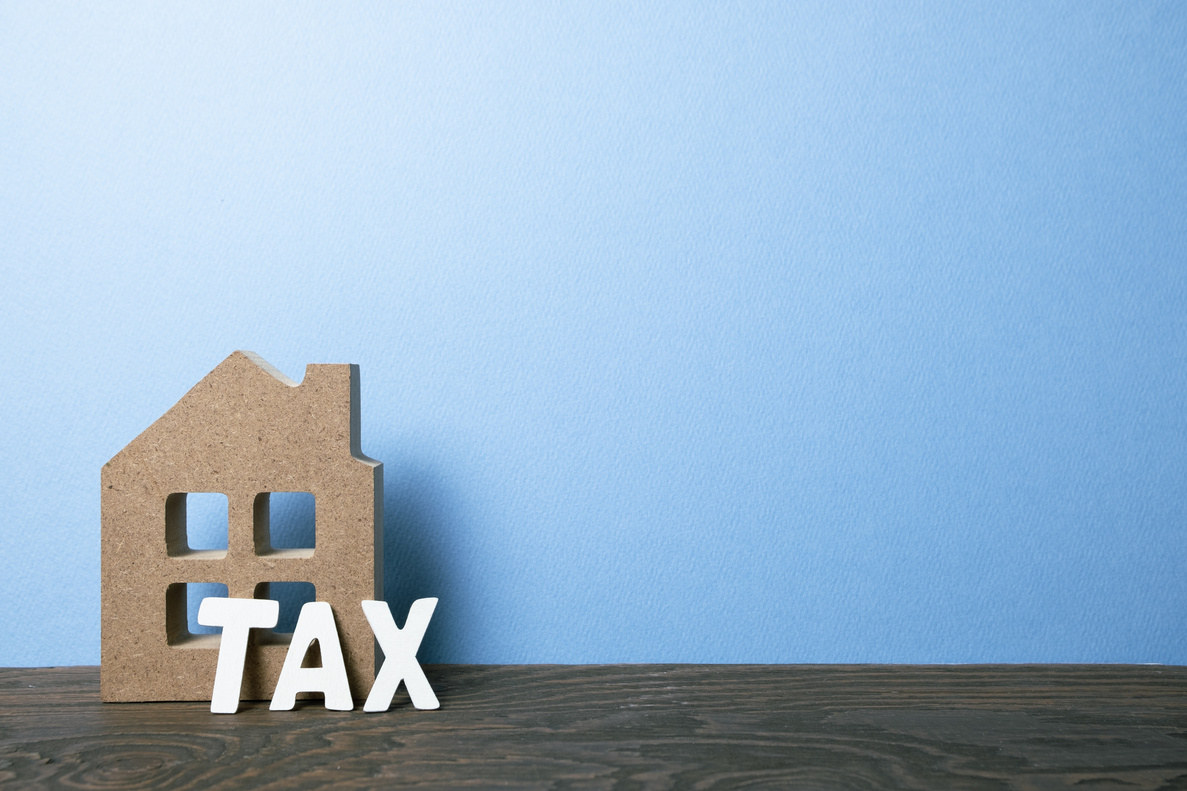 House model with tax on wooden table with blue background. Mortgage or property tax concept